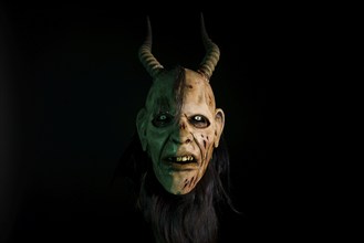 Greenish illuminated mask of a devil with horns, gloomy and threatening atmosphere