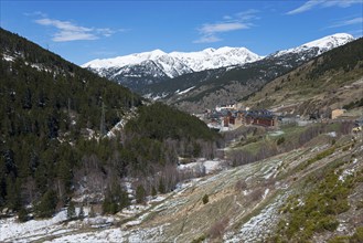 Winterliche Szenerie in einem Tal mit schneebedeckten Bergen, Gebäuden und dichten Wäldern unter