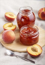 Peach jam in a glass jar with fresh fruits on gray concrete background. side view, close up