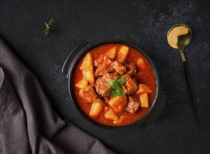 Stew with potatoes, in tomato sauce, with spices and herbs, close-up, no people, on a black