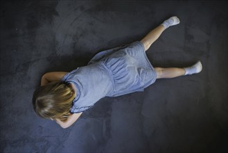 Symbol photo on the subject of tantrums (posed scene) . A little girl lies on the floor and is sad.