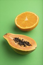 Ripe cut papaya and orange on green pastel background. Side view, close up. Tropical, healthy food,