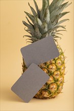 Gray paper business card with ripe pineapple on orange pastel background. Side view, copy space.