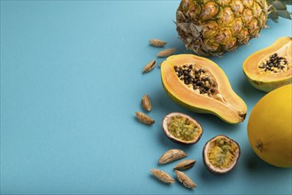 Ripe cut papaya, pineapple, melon, passion fruit, almonds on blue pastel background. Side view,