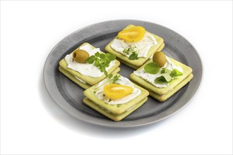 Green cracker sandwiches with cream cheese and cherry tomatoes on gray plate isolated on white