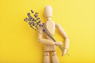 Wooden mannequin holding lavender flowers on yellow pastel background. copy space, isolated,