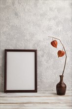 Brown wooden frame mockup with physalis in ceramic vase on gray concrete background. Blank,