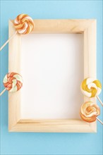 Composition with lollipops and wooden frame on blue pastel background. copy space, top view, flat