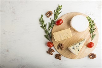 Blue cheese and various types of cheese with rosemary and tomatoes on wooden board on a white