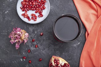 Glass of pomegranate juice on a black concrete background with red textile. Top view, close up,