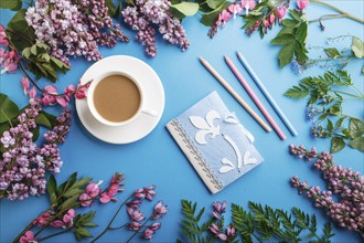 Purple lilac and bleeding heart flowers and a cup of coffee with notebook and colored pencils on