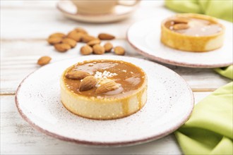 Sweet tartlets with almonds and caramel cream with cup of coffee on a white wooden background and