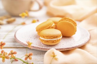 Orange macarons or macaroons cakes with cup of apricot juice on a white wooden background and