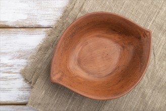 Empty clay brown bowl on white wooden background and linen textile. Top view, close up, flat lay