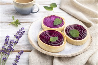 Sweet tartlets with jelly and milk cream with cup of coffee on a white wooden background and linen