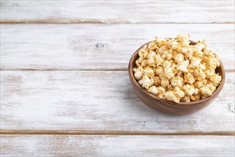 Popcorn with caramel in wooden bowl on a white wooden background. Side view, copy space