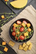 Vegetarian vegetable salad of tomatoes, pumpkin, microgreen pea sprouts on black concrete