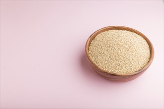 Wooden bowl with raw white quinoa seeds on a pastel pink background. Side view, copy space