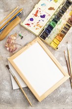 Drawing accessories set: brushes, pencils, watercolor, frame on brown concrete background. Top