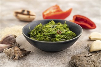 Chuka seaweed salad in blue ceramic bowl on brown concrete background. Side view, close up,