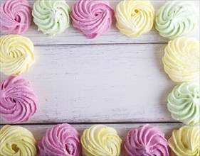 Colorful frame of multicolored meringues on white wooden background. copy space, top view, flat lay