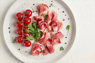 Sliced prosciutto, appetizer, with cherry tomatoes, on a white plate, top view