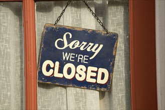 Old fashioned 'Sorry we're Closed' sign in window of closed down village shop