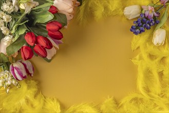 A vibrant spring bouquet of tulips and spring flowers surrounded by yellow feathers on a yellow