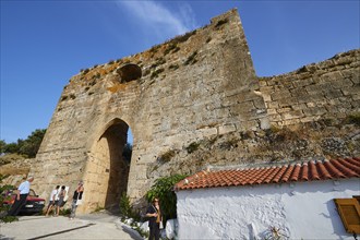 Visitors stroll next to an ancient masonry arch under a blue sky, Koroni, Byzantine fortress,