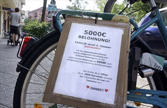 A family draws attention to their search for a flat with a poster mounted on a bicycle. The family