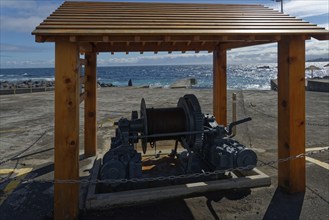 Historic whale towing facility and winch under a wooden canopy with a view of the sea and blue sky,