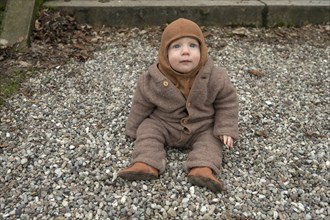 Small child, 8 months, wrapped up warm, sitting on the gravel, Mecklenburg-Vorpommern, Germany,