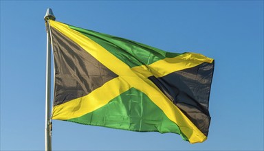 The flag of Jamaica flutters in the wind, isolated against a blue sky