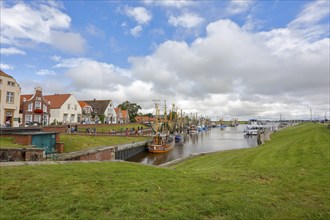 View of historic houses with colourful facades at the old harbour of Greetsiel, with fishing boat,