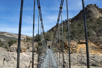 A suspension bridge leads through a rocky gorge with steep walls and green vegetation, Noguera