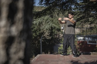 Distant view of a focused man practicing Chi Kung with his eyes closed in the Tree Hugging posture