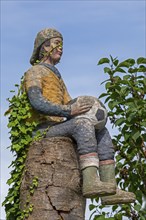 Sculpture of a boy with a football sitting on a tree trunk, Burgstemmen, Lower Saxony, Germany,