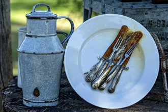 Curious rustic still life, rusty cutlery, old milk can made of enamelled tin, decoration in front