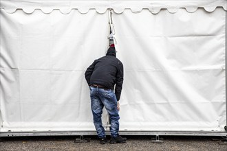 Curiosity, curious man, sticks his head into an event tent, through a gap and watches from outside