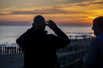 Sunset on the beach of Zoutelande, beach with wooden pile breakwaters, tourists, Zeeland,