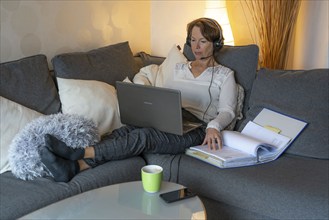 Woman, mid-50s, works from home, with laptop and communicates with colleagues via headset, home