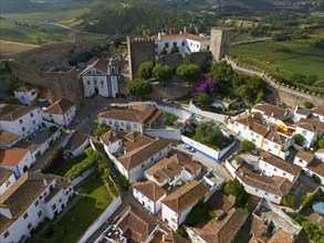 Aerial view of a medieval town with white houses and red tiled roofs, surrounded by city walls and