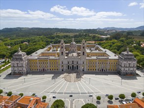 Aerial view of a baroque palace with symmetrical design, surrounded by a green landscape and