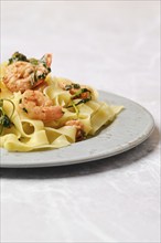 A serving of shrimp fettuccine garnished with fresh herbs is elegantly presented on a gray plate,