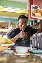 Vendor at a food stall shows thumbs up, looks into the camera, Mercado Central de San José, San