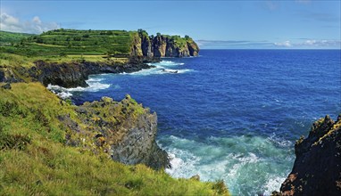 Rugged coastline with steep cliffs and roaring waves breaking the blue sea under a bright sky,