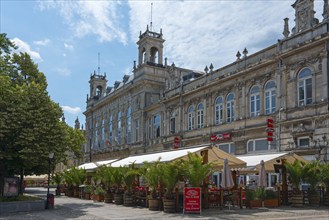 A street café in front of a historic building on a sunny day with blue sky and clouds, Drama