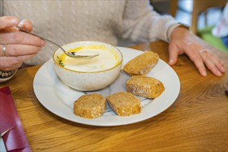 A person spooning a soup served with slices of bread on a white plate, autumn creations, Cafe Kuh,