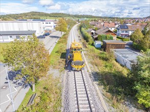 Yellow maintenance vehicle on the tracks, surrounded by trees and residential buildings with a