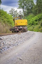 Yellow machine on rails and ballast with trees in the background, track construction, Hermann